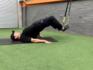 Damien performing a Glute/hamstring bridge using a suspension trainer 